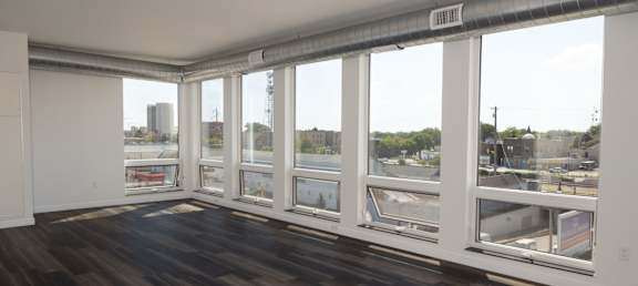 a living room with hardwood floors and a large window with a view of a city at The Landing at 1001 NP, Fargo, North Dakota 58102