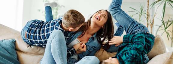 A family of three is lying on a beige couch.
