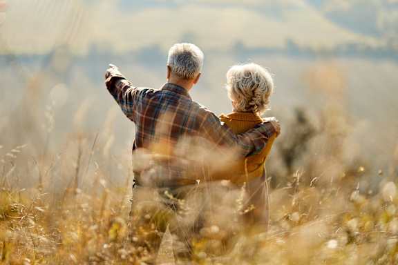 An elderly couple is standing in a field of tall grass.