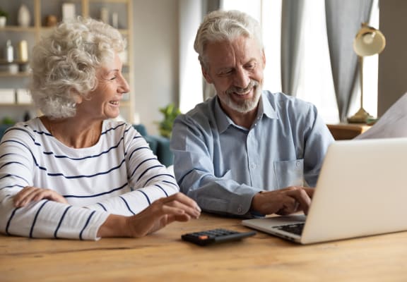 an older couple sitting at a table looking at a laptop