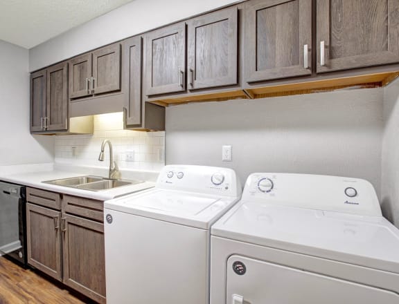 a white washer and dryer in a kitchen with wooden cabinets
