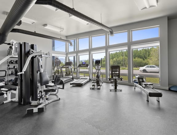 a spacious fitness center with cardio equipment and large windows with a view of a parking lot