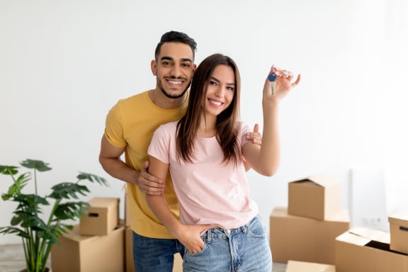 a young couple standing in a room with cardboard boxes and holding a remote control