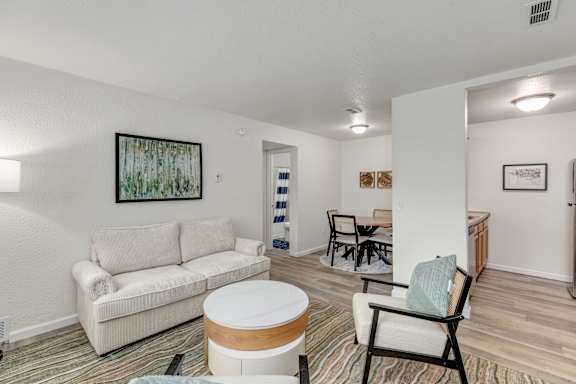 A living room with a white couch and a painting on the wall.