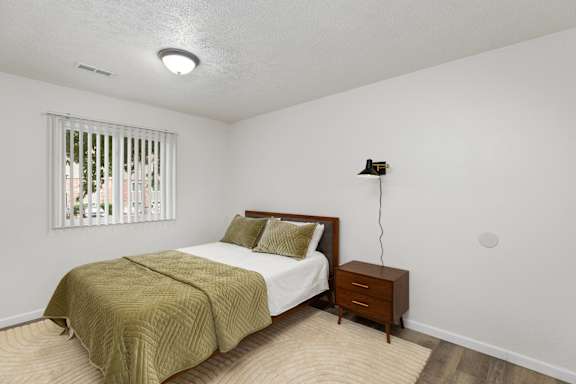 A bedroom with a bed, nightstand, and window.