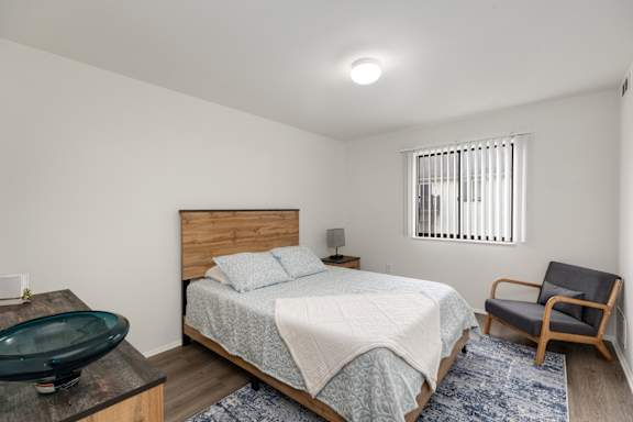 A bedroom with a bed, chair, and window.