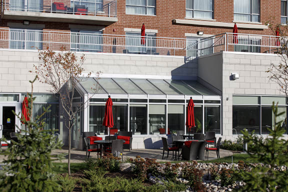 An outdoor patio with tables and red umbrellas in front of a brick building