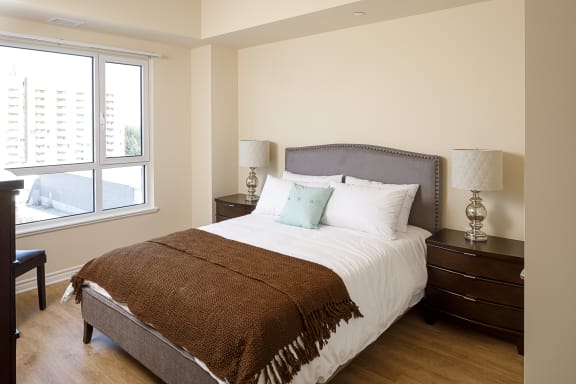 A bedroom with a large window and a bed with a white comforter