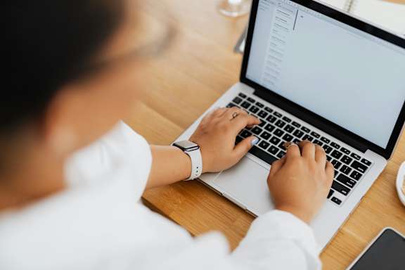 A person is typing on a laptop with a white screen.