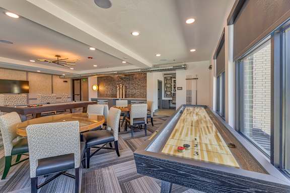 A room with a shaggy carpet and a long table with chairs and a shuffleboard table.