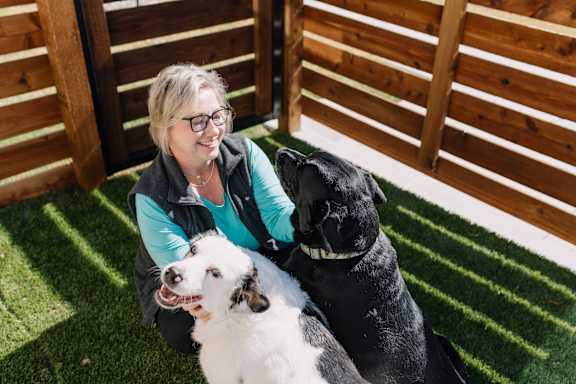 A woman is sitting on the grass with two dogs.