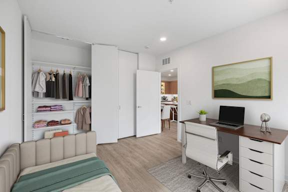 A room with a couch, a desk, and a closet with clothes.