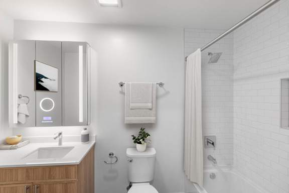 A white bathroom with a toilet, sink, mirror, and a plant.