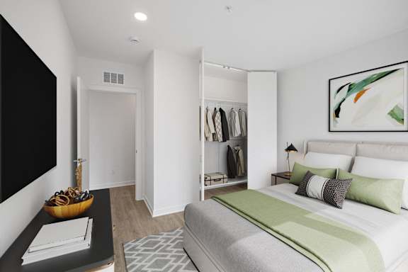 A bedroom with a large bed and a closet with clothes hanging.