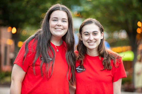 Two women wearing red shirts standing in front of a blurry background.