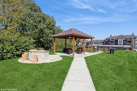 A gazebo is situated in a grassy area with a stone wall and a concrete walkway at Island Club Apartments, Columbus, OH, 43235
