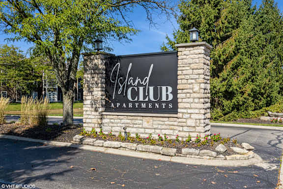 A sign for Island Club Apartments is displayed in front of a tree.