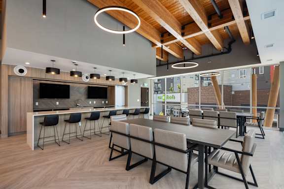 a communal area with tables and chairs and a kitchen with a bar and television