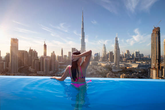 a woman in a infinity pool overlooking the dubai skyline