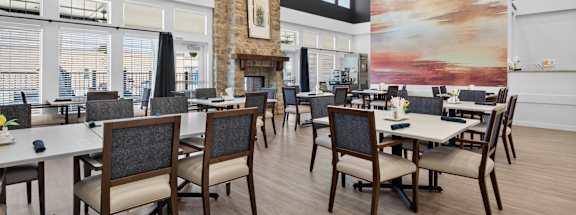 A room with a large painting on the wall and several tables with chairs.