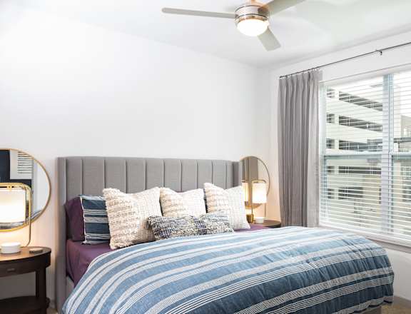 A bedroom with a bed, a ceiling fan, and a window with blinds.