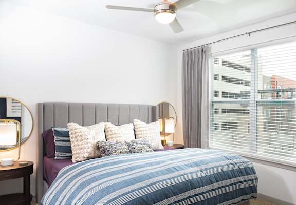 A bedroom with a bed, a ceiling fan, and a window with blinds.