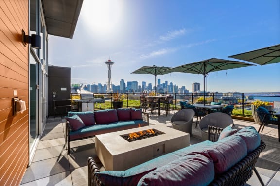 a rooftop patio with couches and chairs and a city skyline in the background