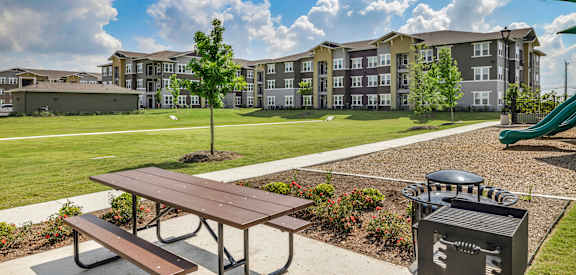 a picnic table with a grill in front of an apartment complex