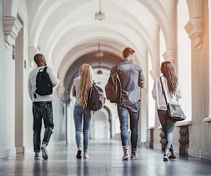 Three people walking down a corridor with arches on the sides.