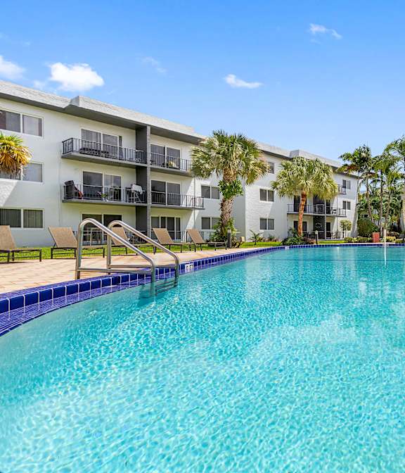 A large swimming pool in front of a building with palm trees.