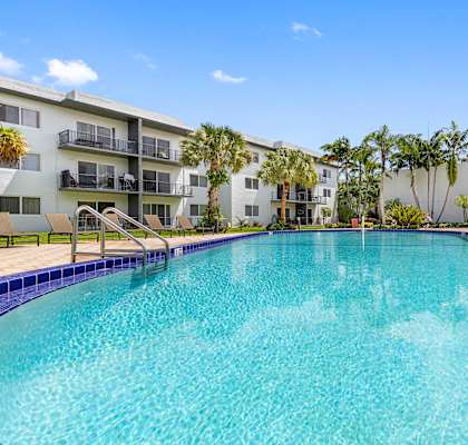 A large swimming pool in front of a building with palm trees.