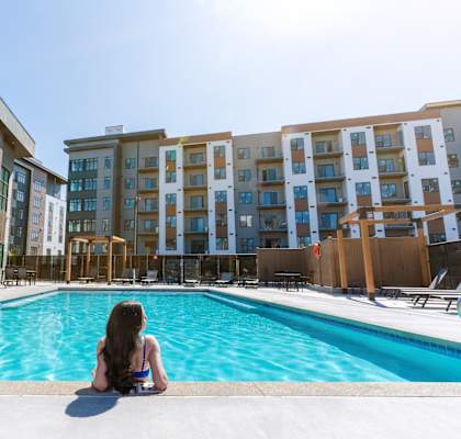 A woman sits by a pool in front of apartment buildings.at Podium Apartments, Calgary, AB