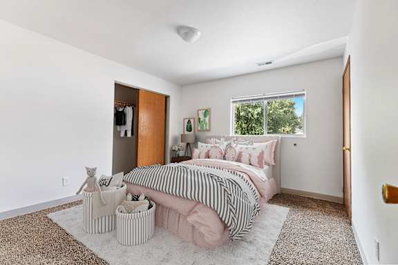 a bedroom with white walls and a pink bed with a black and white striped comforter