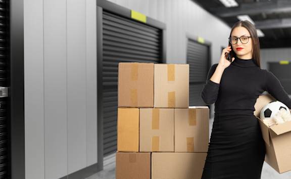 A woman in a black dress is holding a cardboard box with a panda on it while talking on the phone.