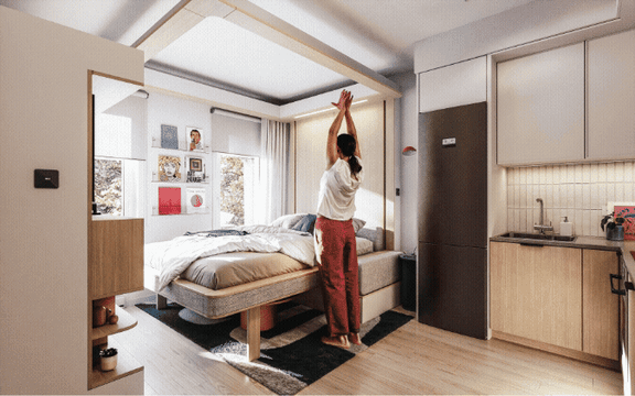 A woman is stretching in a well-lit, modern bedroom with a large bed and a kitchen area.