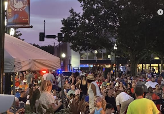 A large crowd of people are gathered in a park at dusk.