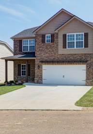 A two-story house with a garage is surrounded by a grassy lawn and a sidewalk.