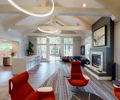 The resident lounge with a fireplace, couches, decorations, plush red chairs, coffee tables, and a resident kitchen with a coffee bar, sink, refrigerator, and dishwasher at Portsmith Apartments. 