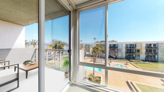 A balcony with a table and chairs overlooks a pool and buildings. at Marina Harbor, Marina del Rey, California