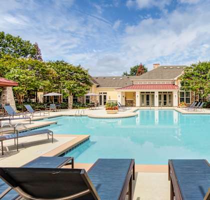 A large swimming pool with lounge chairs and a house in the background.