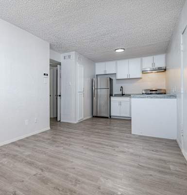 an empty living room and kitchen with white walls and wood flooring
