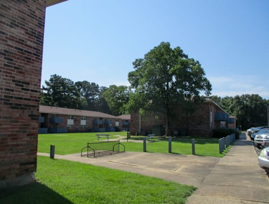 A park area with a picnic table and a tree in front of a brick building.