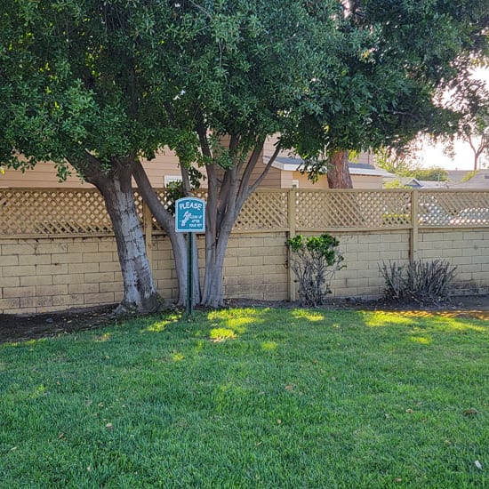 a sign in a yard with a tree and a fence in the background