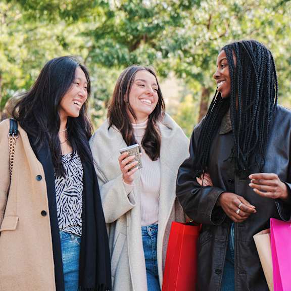 Three women are walking together while holding shopping bags.