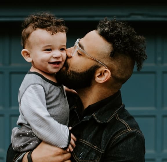 Dad Kissing Young Son While Holding In Arms