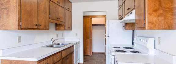 A kitchen with brown cabinets and white appliances. Fargo, ND Carr Apartments
