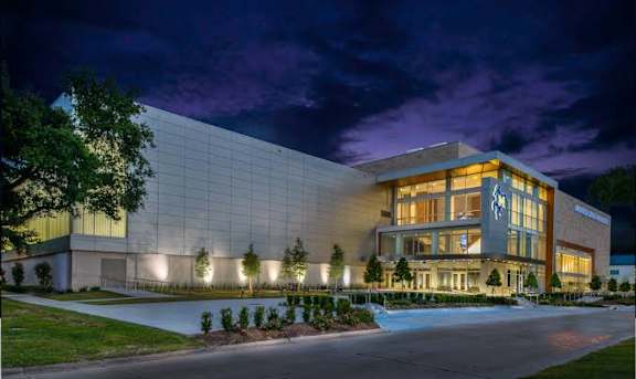 A modern building with a glass facade and a large entrance is illuminated at night.