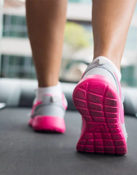 a woman wearing pink sneakers walking on a treadmill