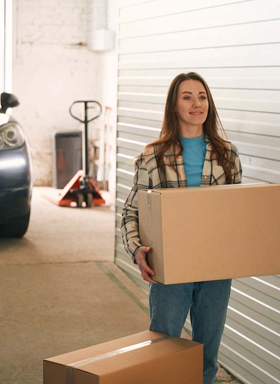 A woman is carrying a box in a garage.