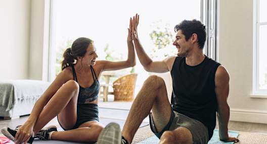 A man and a woman are giving each other a high five while sitting on yoga mats.